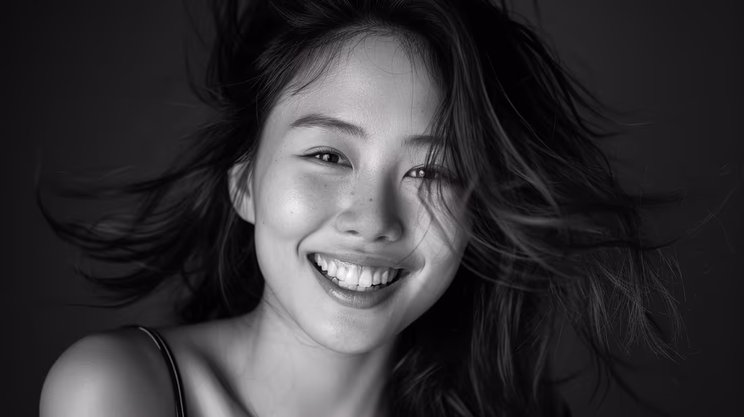 Close-up black and white portrait of a young woman smiling with wind-blown hair.